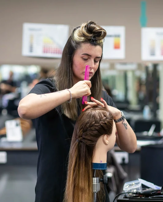 Hairstyling student carefully styling a mannequin’s hair in a salon. Hairstyling student carefully styling a mannequin’s hair in a salon.